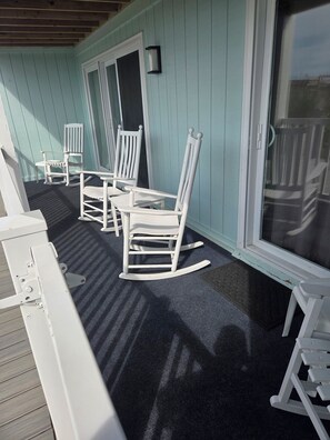 Une véranda couverte avec des fauteuils à bascule blancs et une table, une porte et une fenêtre.