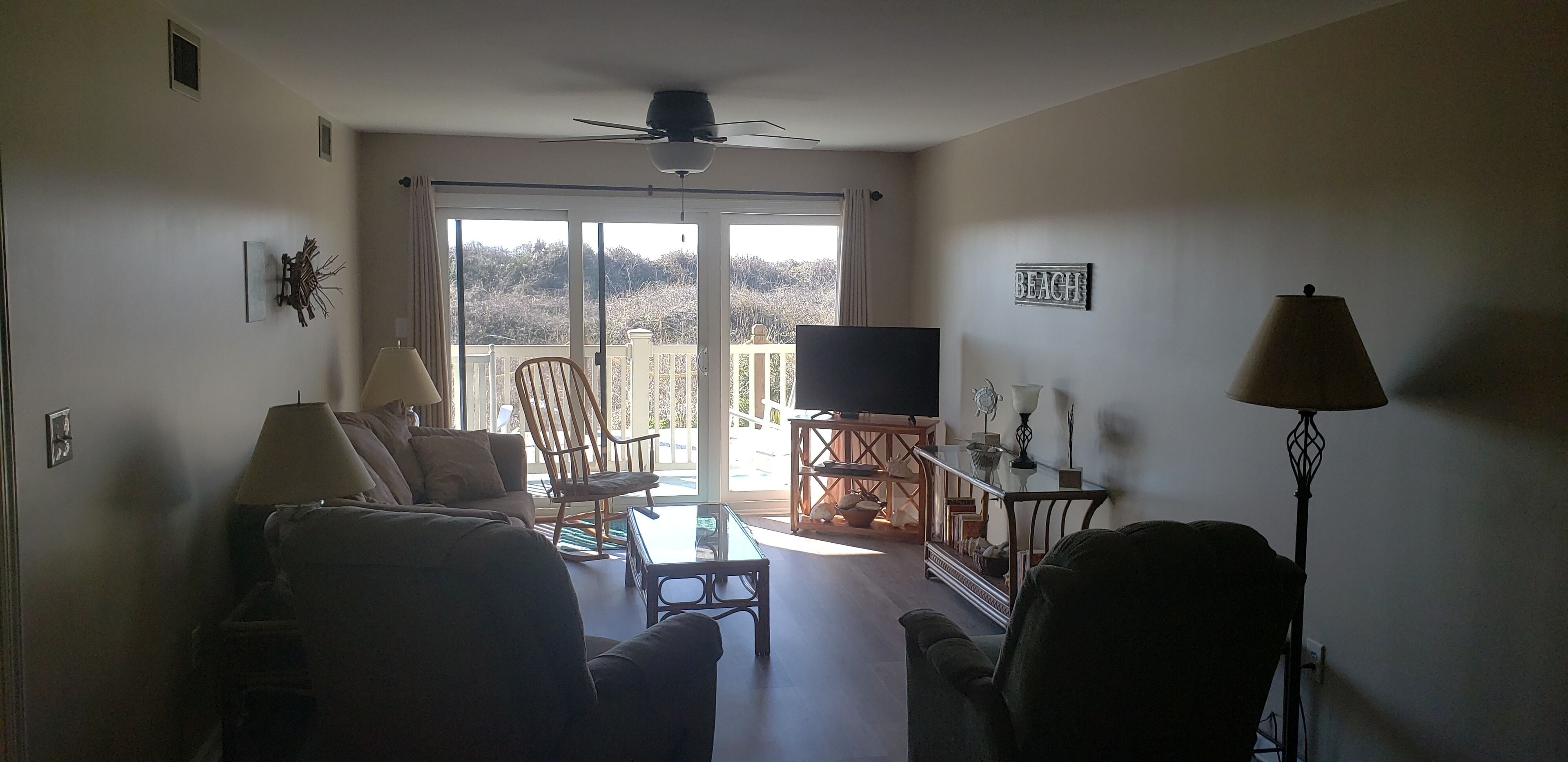 A living room with a sofa, armchairs, a coffee table, a TV, and a balcony with a view.