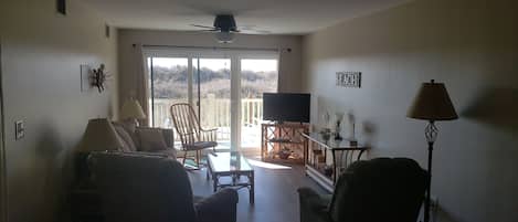Una sala de estar con sofá, sillones, una mesa de centro, televisor y un balcón con vistas.