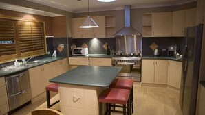A modern kitchen with a central island, built-in appliances, and a dining area with benches. - Stanthorpe Country Resort, 6 bedrooms for 12 guests (Stanthorpe)
