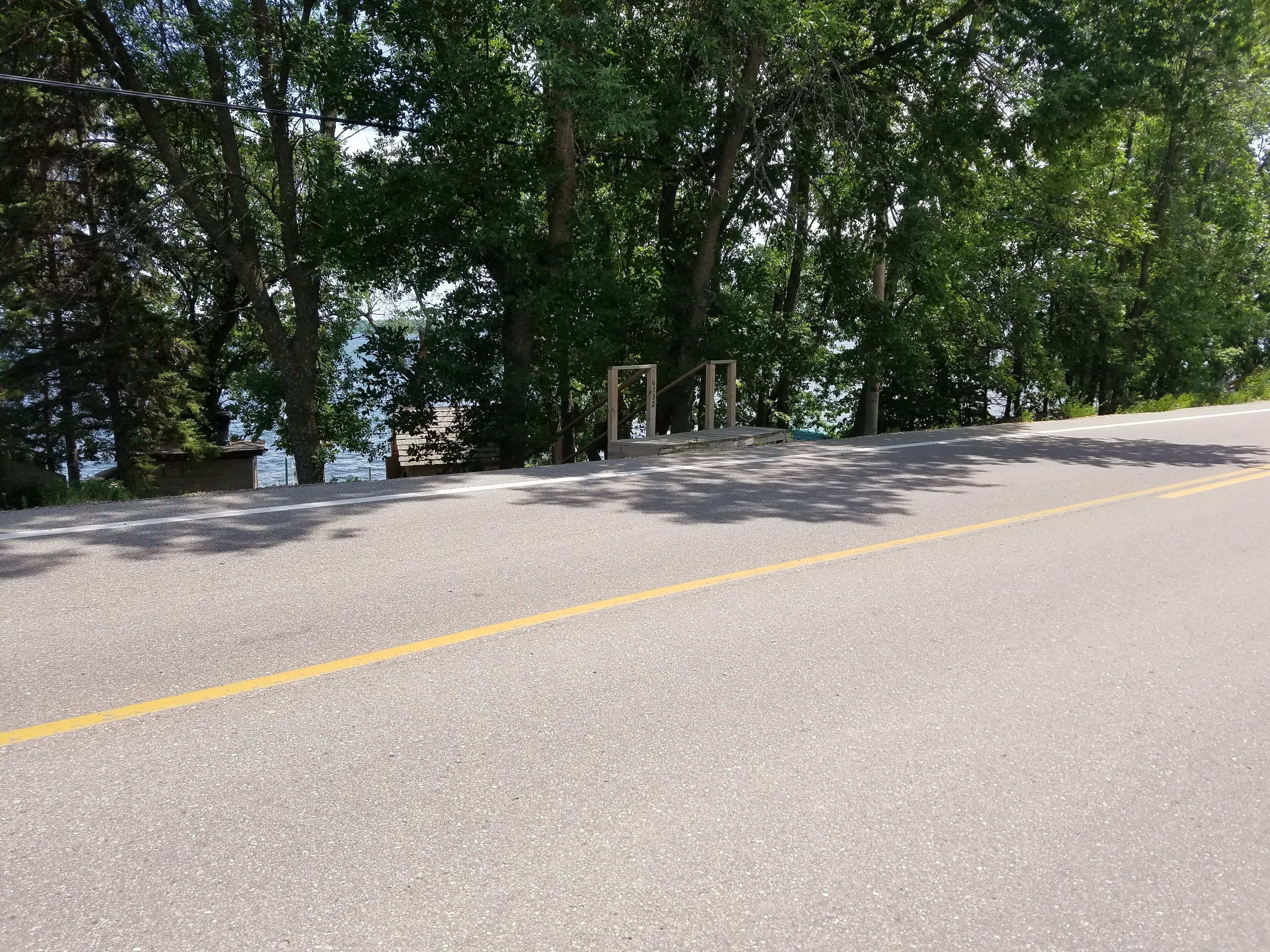 A paved road with a yellow dividing line, surrounded by trees and a body of water in the background.