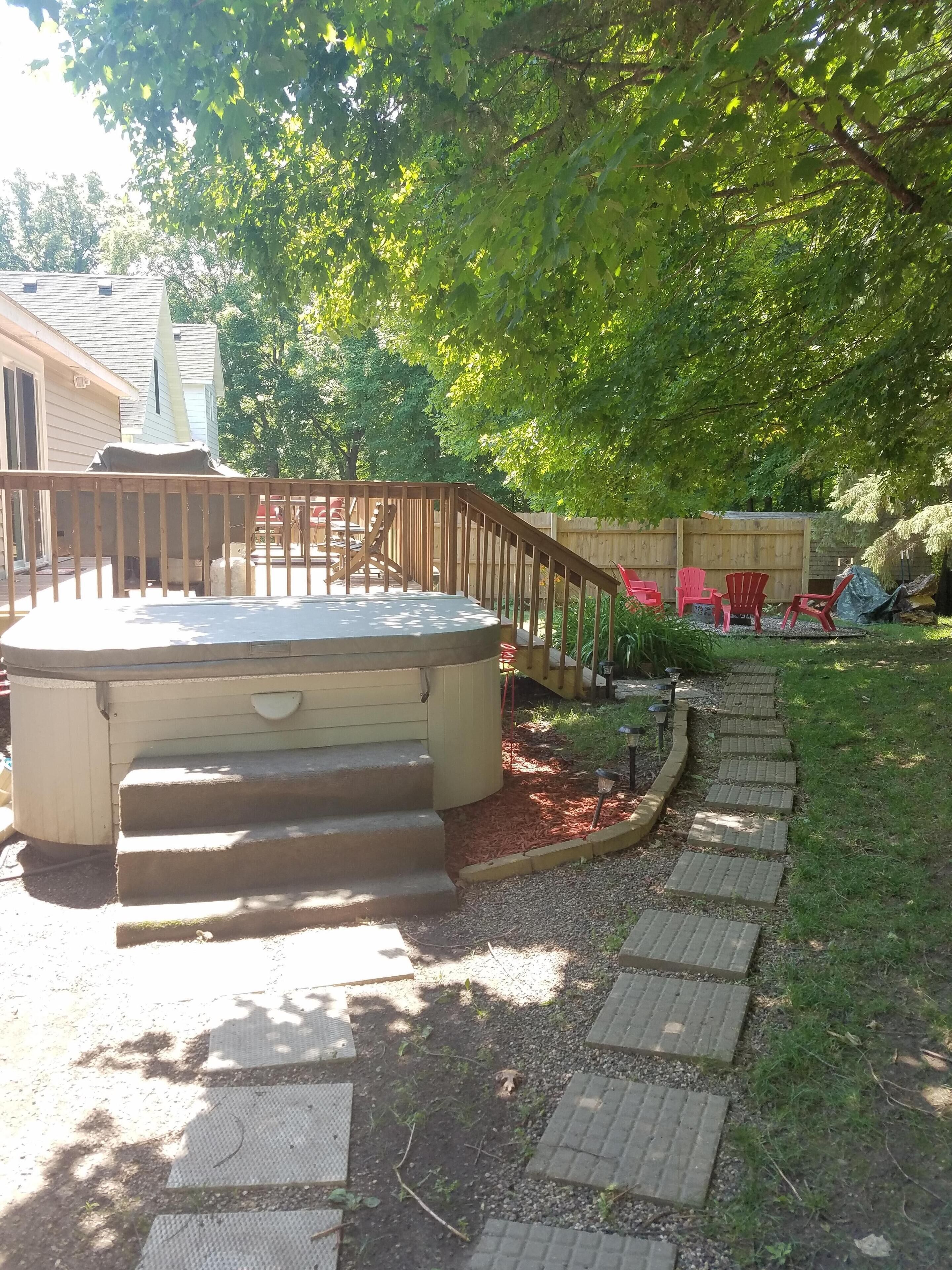 A backyard with a hot tub, a wooden deck, and a brick pathway.