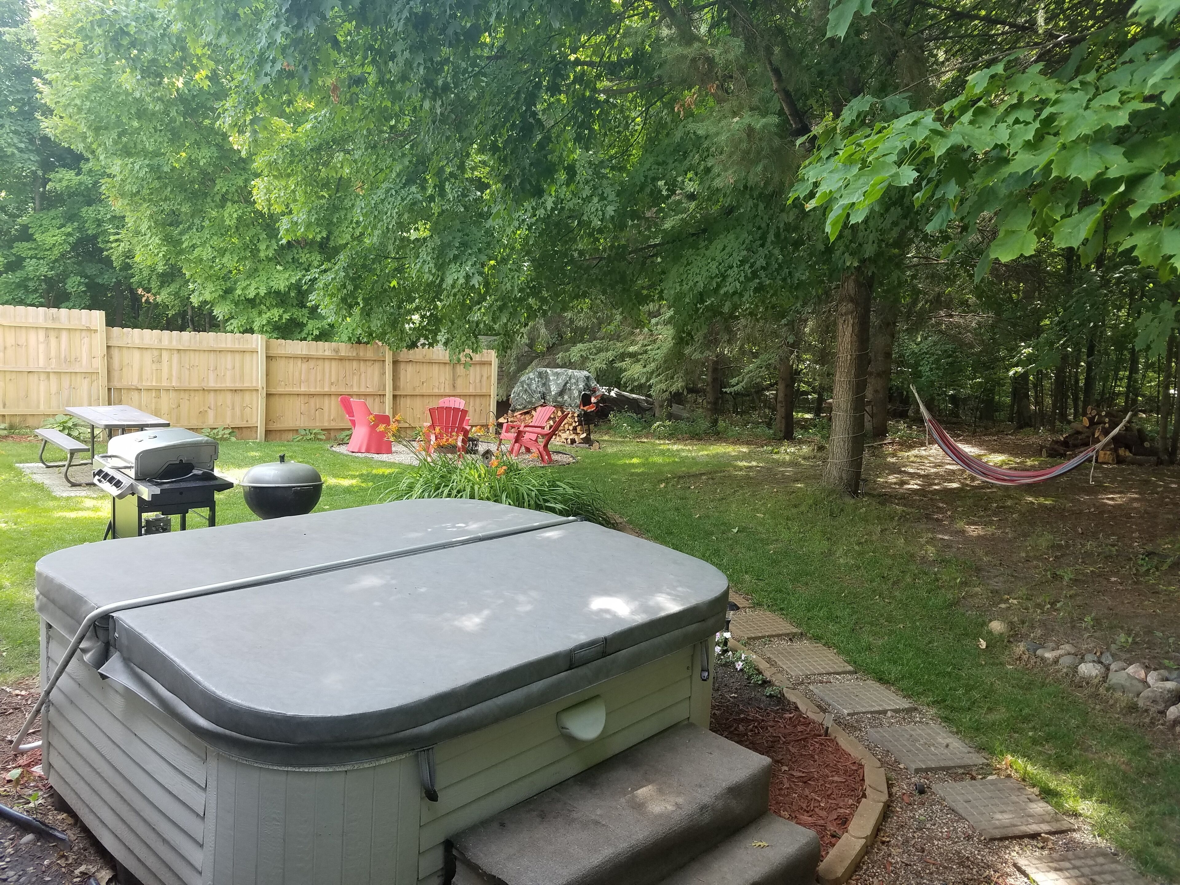 A backyard with a hot tub, a barbecue grill, and red chairs.