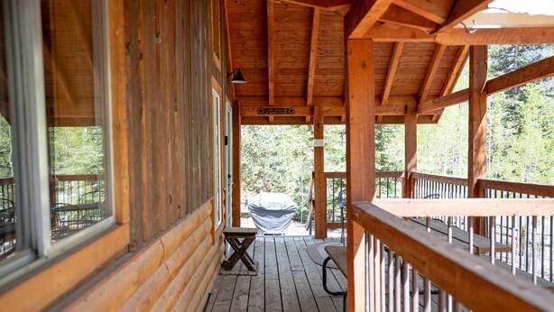 Una cabaña de madera con un porche cubierto, un letrero de bienvenida y una zona de parrilla techada.