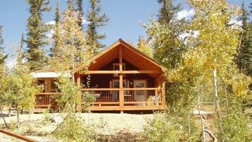 Une cabane en bois dotée d’un porche, entourée d’arbres et d’une clôture en bois.