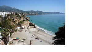 Une plage côtière bordée de falaises rocheuses, une mer bleue et limpide, et quelques personnes profitant du soleil.