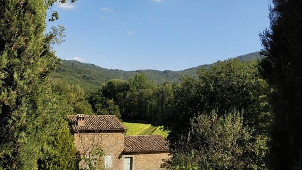 A stone house with a swimming pool, surrounded by trees and hills.