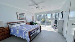 A bedroom with a bed, a nightstand, a dresser, a ceiling fan, and a large window offering a view of the outdoors. - Pet Friendly, Magnificent Ocean Views, A minutes' Easy Stroll To The Beach (Black Head)