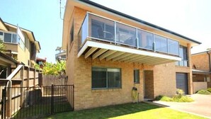 A modern two-story house with a large glass balcony, a brick facade, and a well-maintained lawn. - Pet Friendly, Magnificent Ocean Views, A minutes' Easy Stroll To The Beach (Black Head)