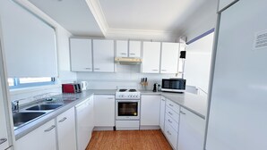 A compact kitchen with white cabinets, a stove, a microwave, and a sink. - Pet Friendly, Magnificent Ocean Views, A minutes' Easy Stroll To The Beach (Black Head)