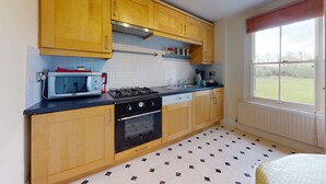 Une cuisine avec des meubles en bois, un four à micro-ondes, une cuisinière et une fenêtre donnant sur l’extérieur.