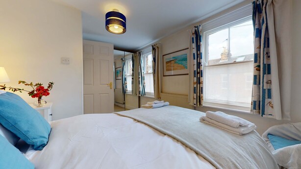 Une chambre d’hôtel avec un grand lit, une table de chevet avec une lampe, un vase de fleurs et une fenêtre avec des rideaux.