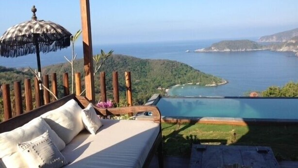 A balcony with a wooden railing, a cushioned sofa, and a patterned umbrella.