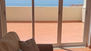 Un salon avec un canapé et une vue sur la mer, visible à travers de grandes portes vitrées.