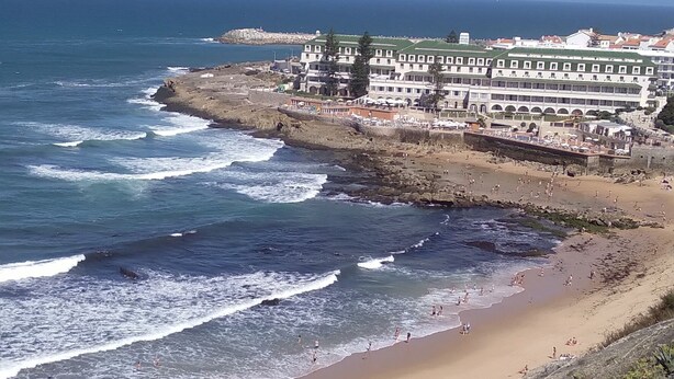 Une vue côtière avec une plage, des vagues et un ensemble de bâtiments en arrière-plan.