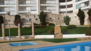 Une piscine dont la profondeur est indiquée à 1,00 mètre, entourée d’un espace aménagé avec de la pelouse, des arbustes et un mur en pierre.