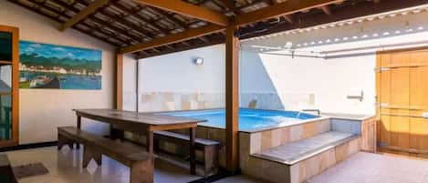 A covered outdoor area with a pool, a wooden table, and benches.