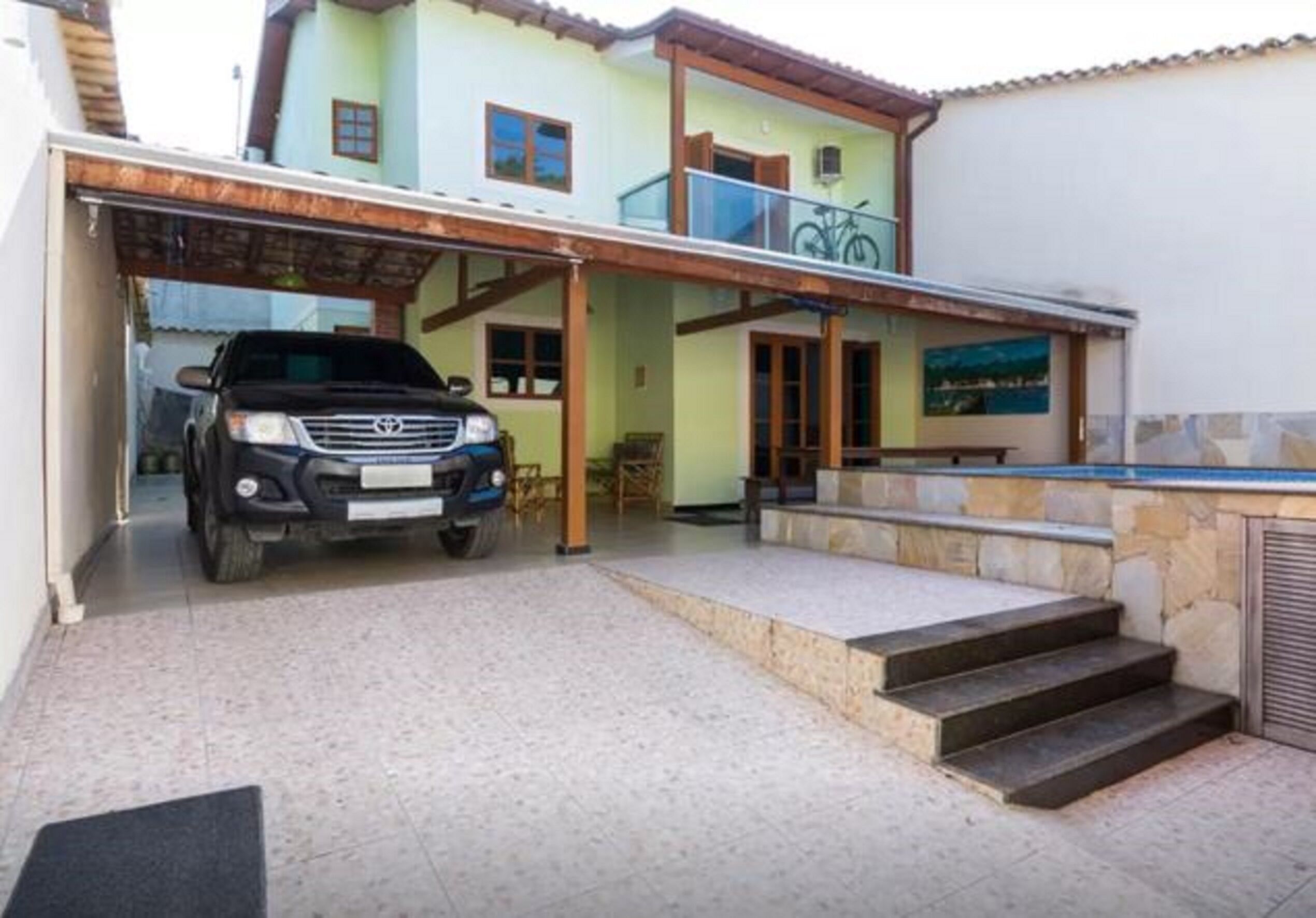 Une maison à deux étages dotée d’un abri-voiture fermé, d’un balcon et d’un petit espace piscine.
