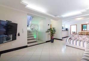 A spacious living area with a flat-screen TV, a staircase with green lighting, a potted plant, and a striped sofa. - House in the center of Paraty with swimming pool. (PARATI)