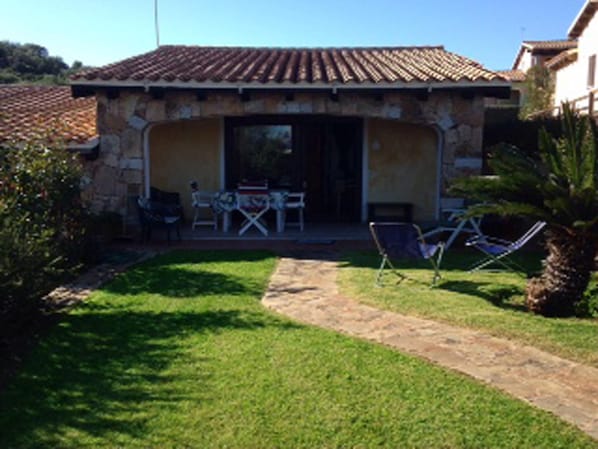 A stone house with a tiled roof, a covered patio with outdoor furniture, and a well-maintained lawn.