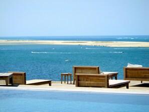A poolside area with wooden lounge chairs and a view of the ocean and beach. - Bright Standing apartment close to the ocean, partial ocean view  (Biscarosse Plage)