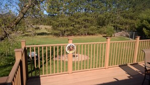 A wooden deck with a metal railing, a thermometer indicating a temperature of 70°F, and a view of a grassy yard with trees and a fence in the background.