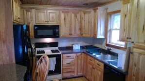 A kitchen with wooden cabinets, a black microwave, a stove, a sink, and a window.
