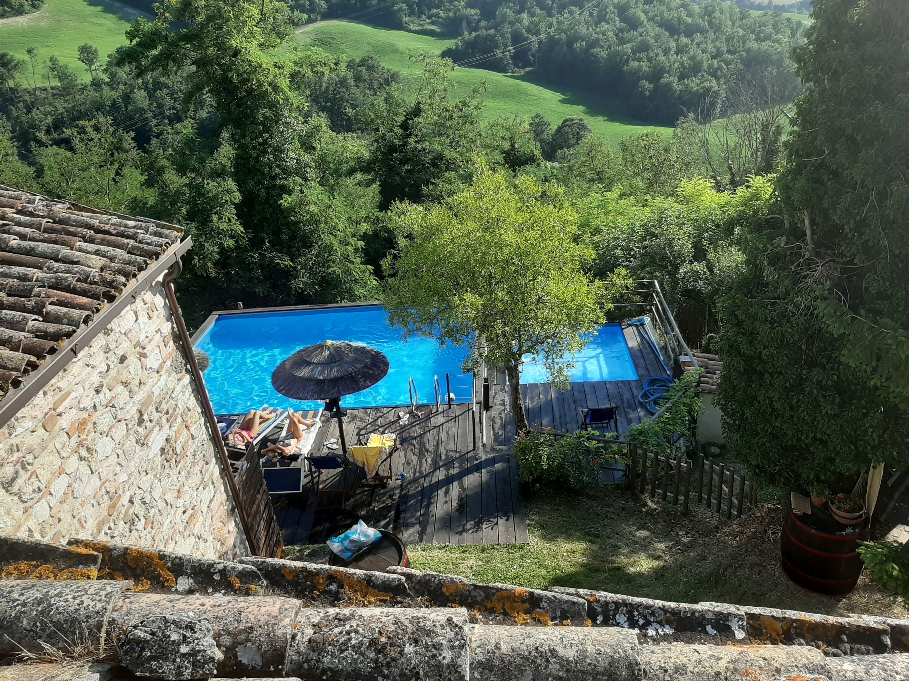 Area piscina con deck in legno, lettini e un ombrellone grande.