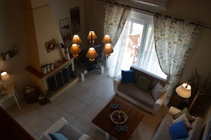 A cozy living room with a sofa, a coffee table, and a fireplace. There are decorative items on the mantel and a window with curtains.
