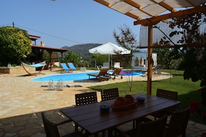 Un área de piscina con sillas de descanso, una mesa con mobiliario exterior y una pérgola que proporciona sombra.
