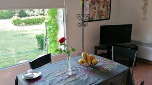 A dining area with a table set for two, a vase with flowers, and a fruit bowl. - HOLIDAY COTTAGE FURNITURE (Saint-Michel-De-Fronsac)
