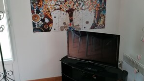 A room with a tiled floor, a black entertainment unit, and a wall-mounted TV. - HOLIDAY COTTAGE FURNITURE (Saint-Michel-De-Fronsac)