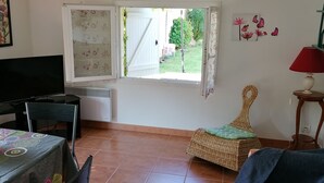 A room with a dining table, chairs, a sofa, a window with a view of the garden, and a lamp. - HOLIDAY COTTAGE FURNITURE (Saint-Michel-De-Fronsac)