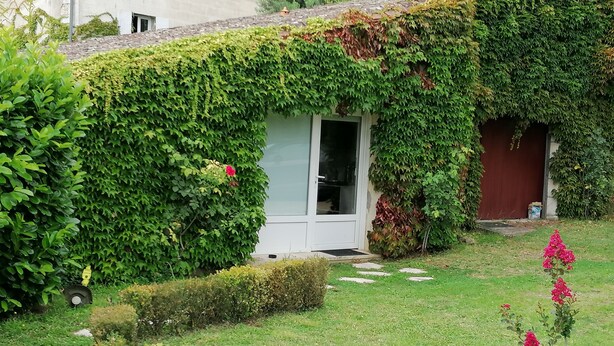 A house with a green ivy-covered exterior, a white door, and a small garden with a pink flower. - HOLIDAY COTTAGE FURNITURE (Saint-Michel-De-Fronsac)