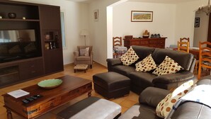 Een woonkamer met een bank, een voetenbankje, een houten salontafel en een tv-meubel.