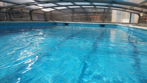 Een binnenzwembad met helderblauw water, een overdekt dak en een zwembadterras.