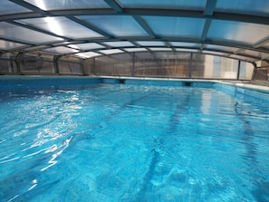 An indoor swimming pool with clear blue water, a covered roof, and a poolside area.