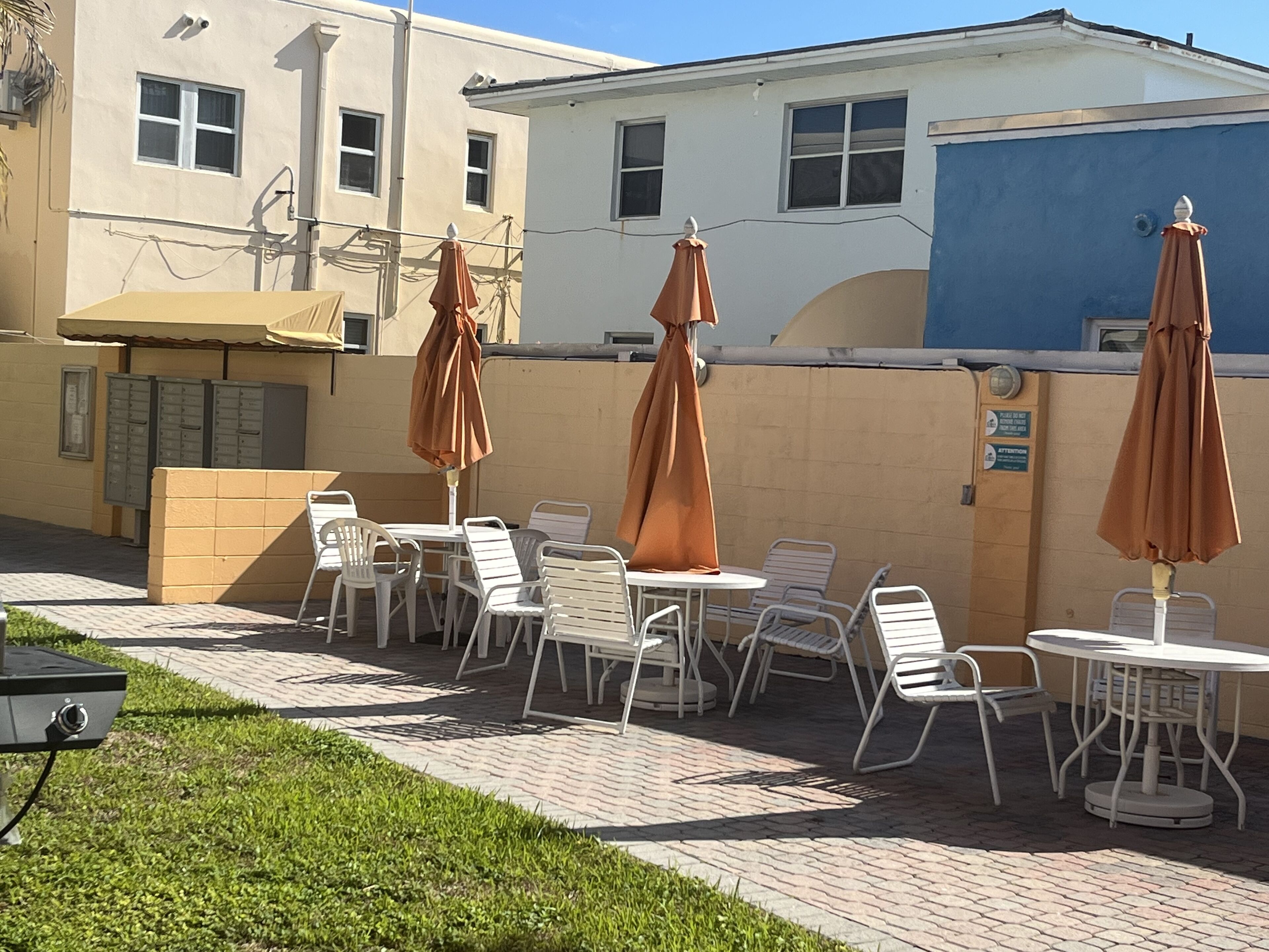 Outdoor seating with umbrellas, a brick pathway, and a building with multiple windows and a blue wall.