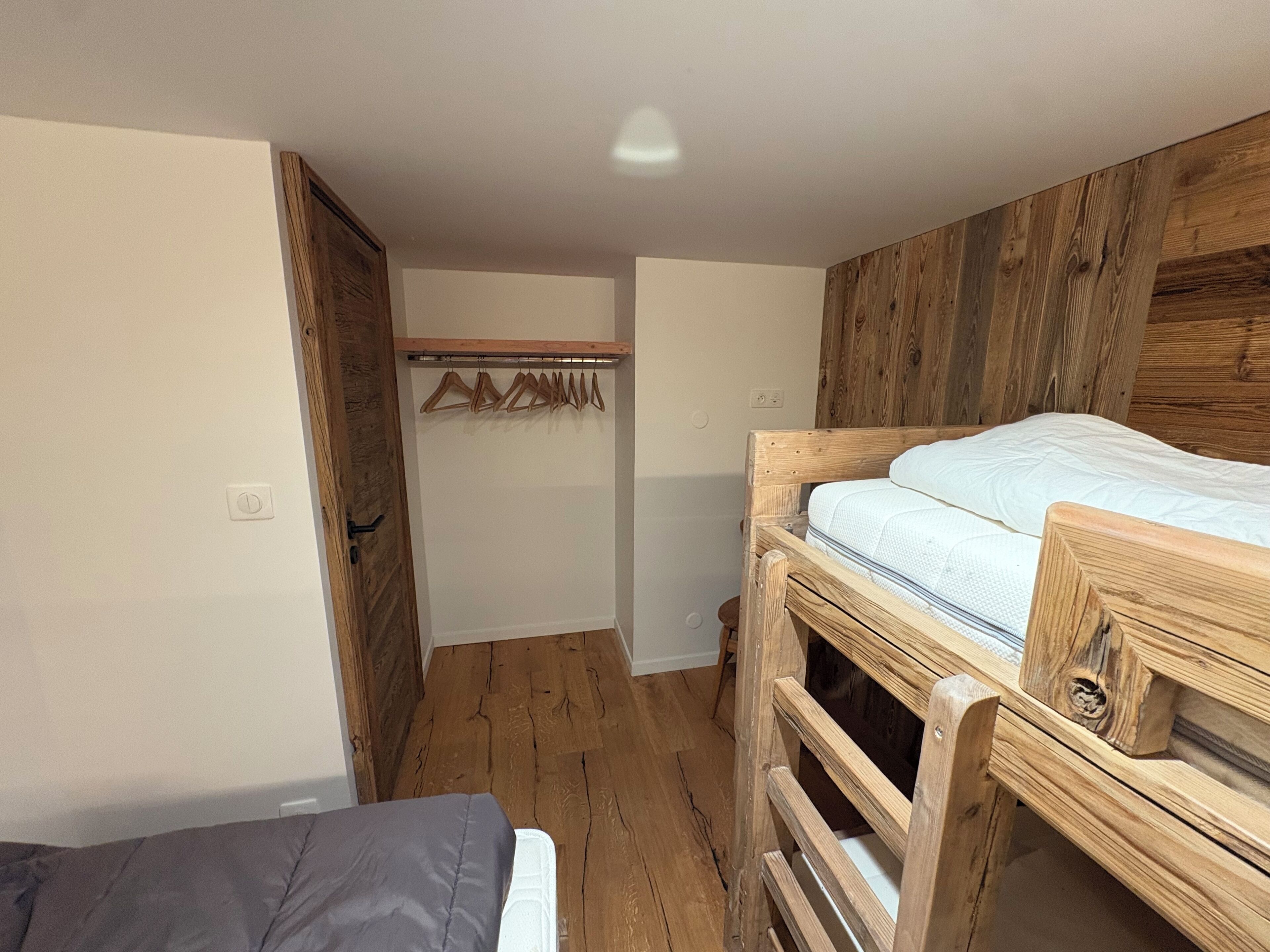 Une petite pièce, de taille modeste, comprenant un lit superposé et un lit simple. On y trouve une armoire en bois et un porte-manteau avec des cintres.
