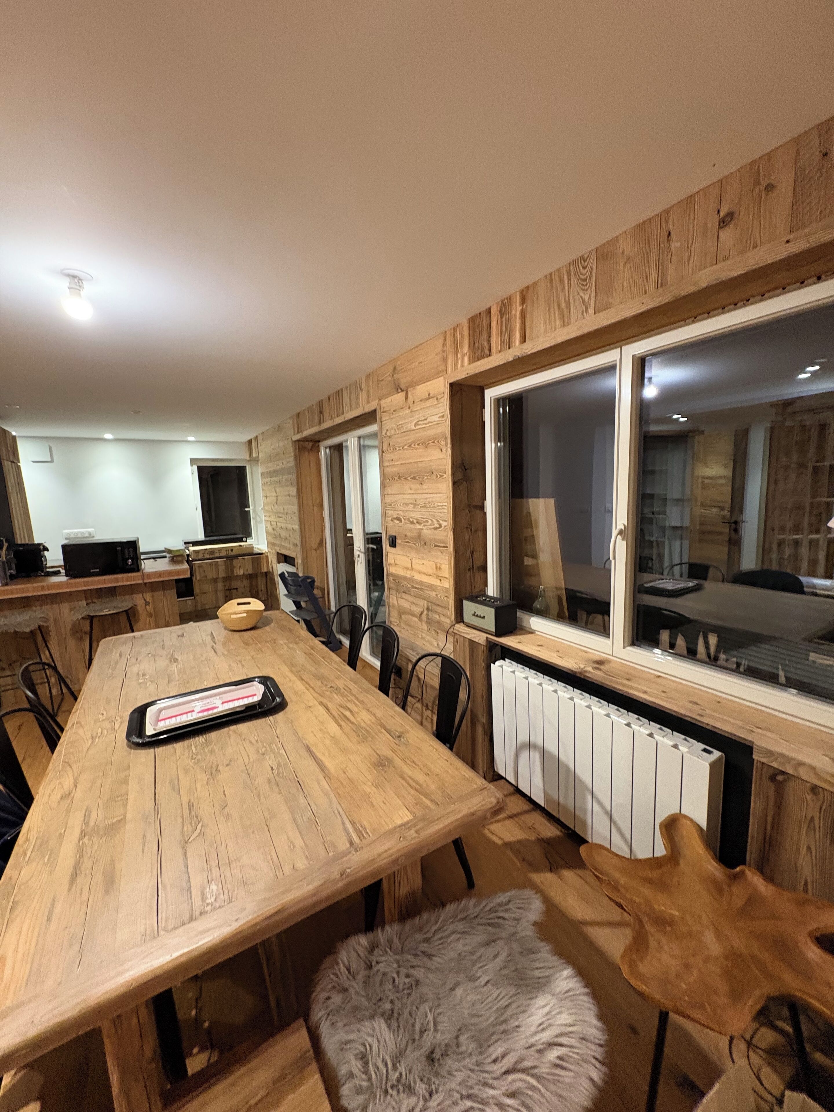 A modern kitchen with wooden cabinetry, a large dining table, and a view through the windows.