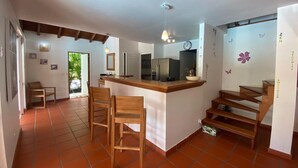 A kitchen with a central island, wooden chairs, a staircase, and a view of the outdoors.