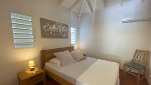 A bedroom with a bed, bedside table, lamp, chair, and artwork on the wall.