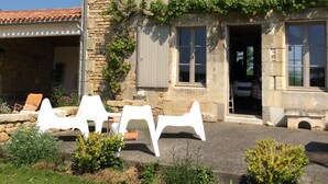 A stone building with a tiled roof, a chimney, and a balcony. There are white plastic chairs and a table outside. - Charming house in the countryside close to the sea (Saint-Cyr-En-Talmondais)