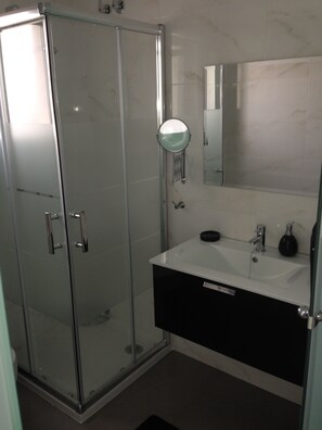 A modern bathroom with a glass shower enclosure, a white sink with a black cabinet, and a mirror above the sink.