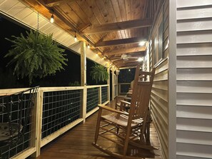 En træterrasse med gyngestol og bord, omgivet af gelænder og plantekasser.