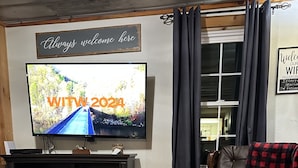 A living room with a fireplace, a leather sofa, a television, and a coffee table with a remote control and a book. - Pet friendly,cozy cabin near Tail of the Dragon.Paved driveway & covered parking (Robbinsville)