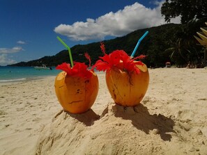 Two coconut drinks on a sandy beach with a clear sky and a mountain in the background. - VILLAS 7 people 130 (victoria)