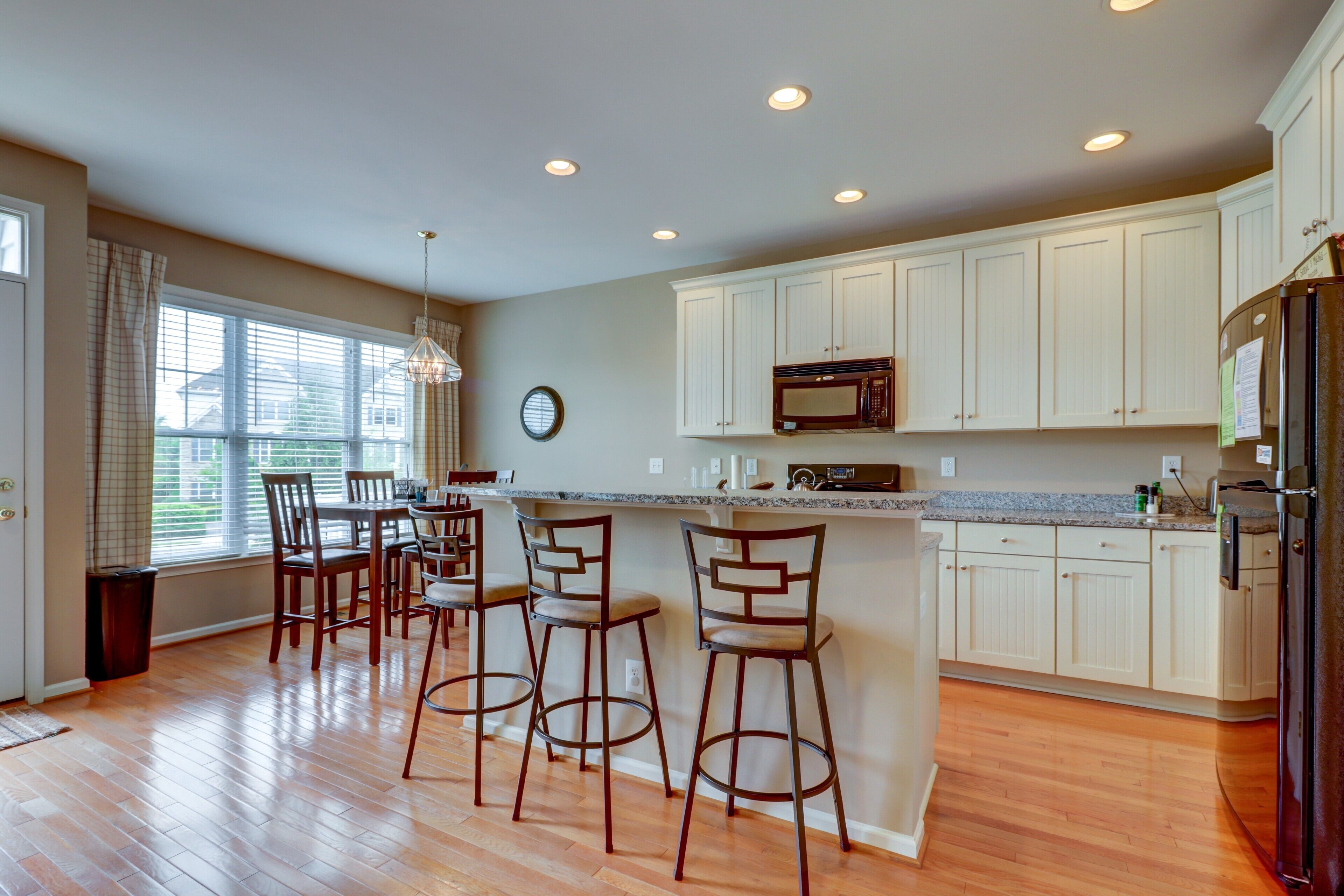 A modern kitchen with wooden flooring, white cabinets, a granite countertop, and a dining area with bar stools.