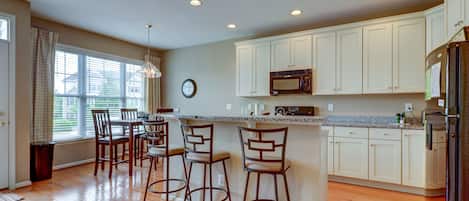 A modern kitchen with wooden flooring, white cabinets, a granite countertop, and a dining area with bar stools.
