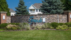 Eine Steinsäule mit der Aufschrift "Grande" in blauer Schrift, umgeben von Grünpflanzen und einem Haus im Hintergrund.